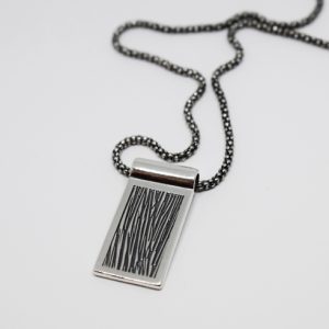 Silverhalsband med gravyr och svartoxidering på vit bakgrund